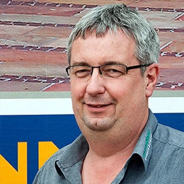 Mittelalterlicher Mann mit Brille lächelt vor Werbetafel, Porträtfoto für Unternehmenswebseite.